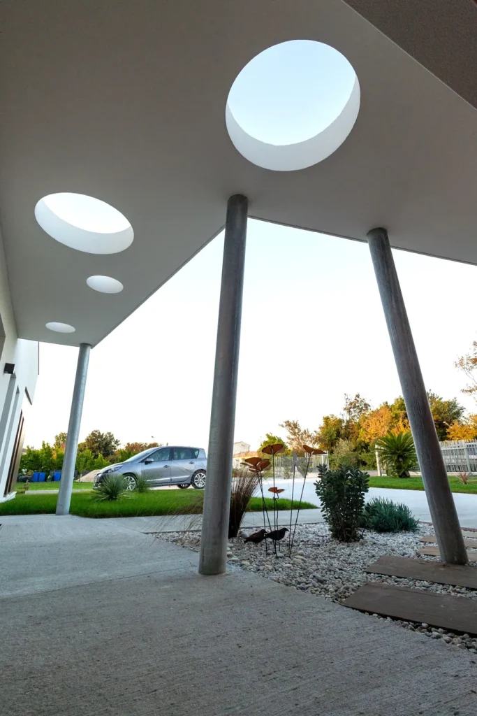 Auvent percé de puits de lumière sur poteaux inclinés, maison contemporaine